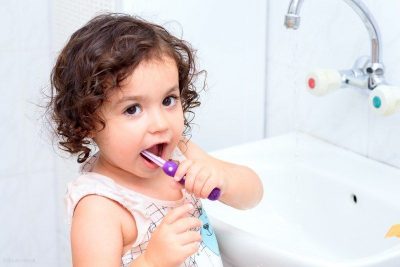 cute little girl brushing teeth at sink